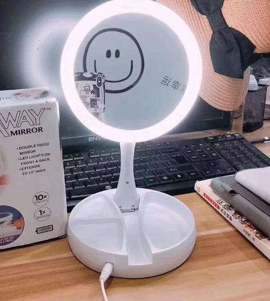 Lighted makeup mirror on a desk with a keyboard and stationery items in the background