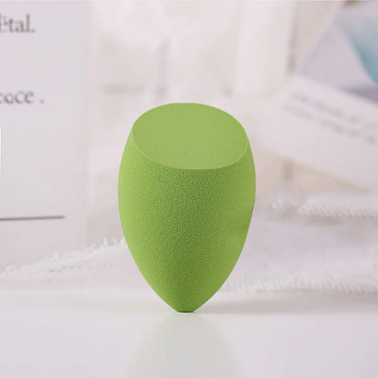 Green makeup sponge on a white surface with a blurred background