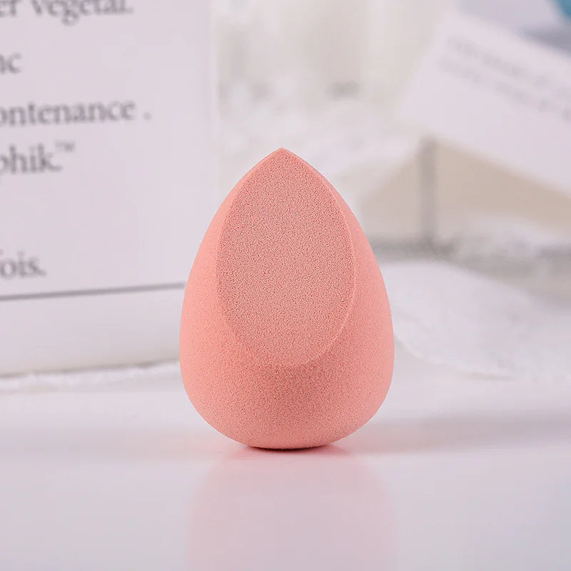 Pink makeup sponge on a light surface with blurred text in the background