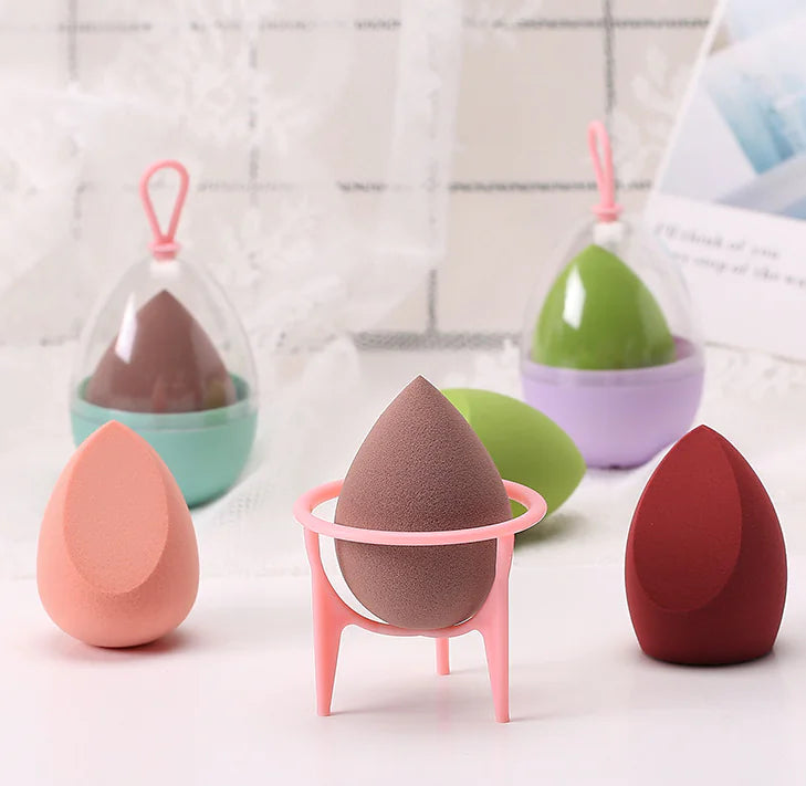 Set of colorful makeup sponges with stands on a white surface.