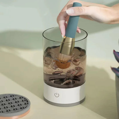 Hand using a brush to clean seashells inside a small cylindrical device on a light surface.